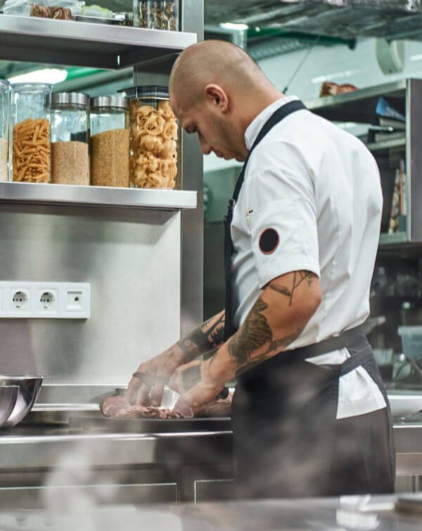 Koch beim Zubereiten von Fleisch in der Produktionsküche von STREET-KITCHEN